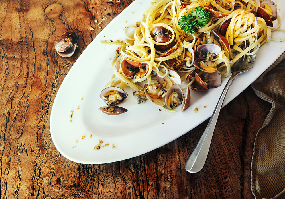 An image rendering of a plate on a wooden table with pasta, mussels and a fork in it.