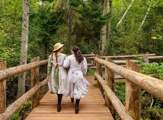 Two girls in traditional clothing walking along the a wooden bridge in PEI National Park
