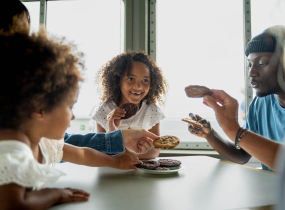 A family shares a plate of cookies around a table.